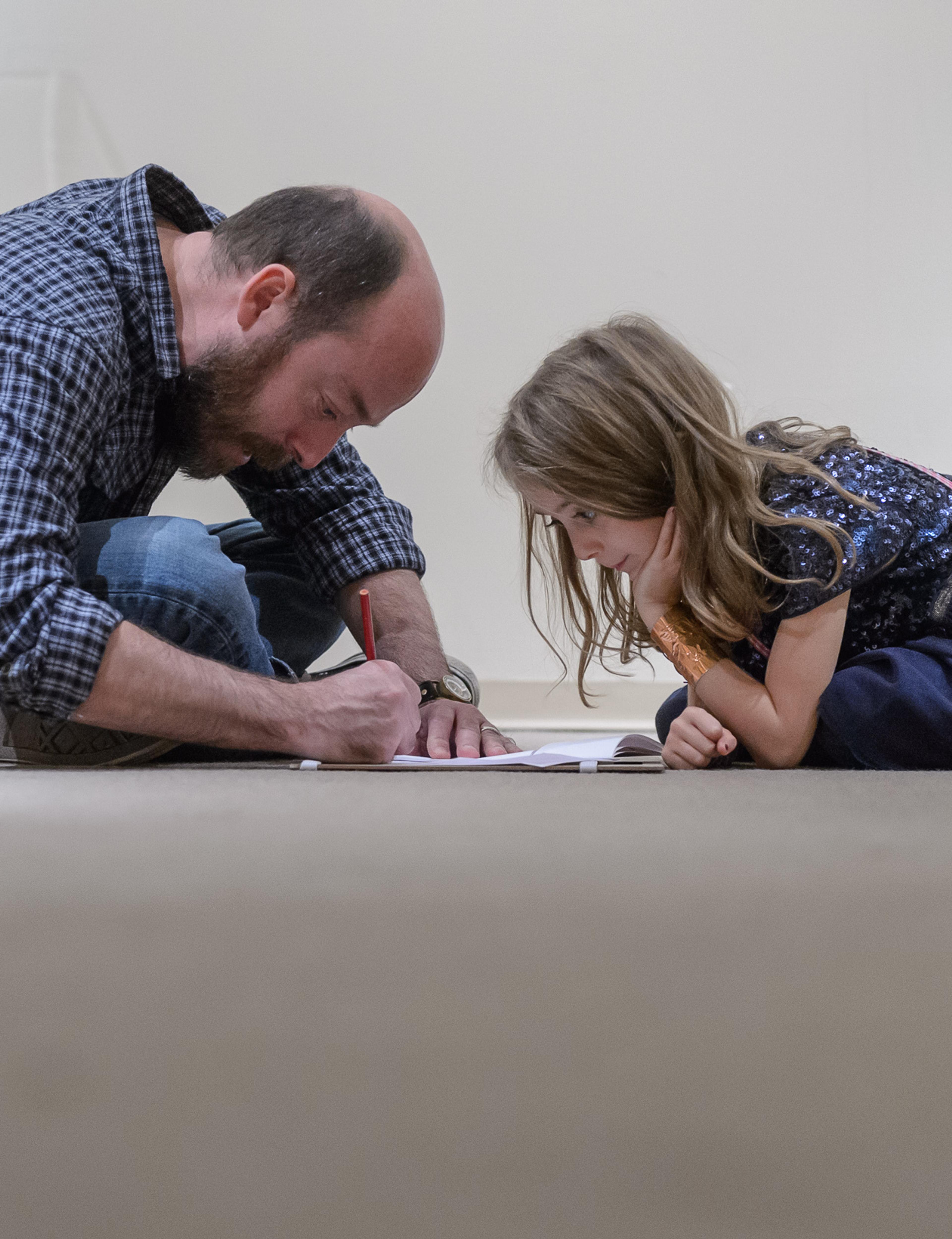 A mid-aged man and a young girl huddle together on the floor engrossed in an activity together.
