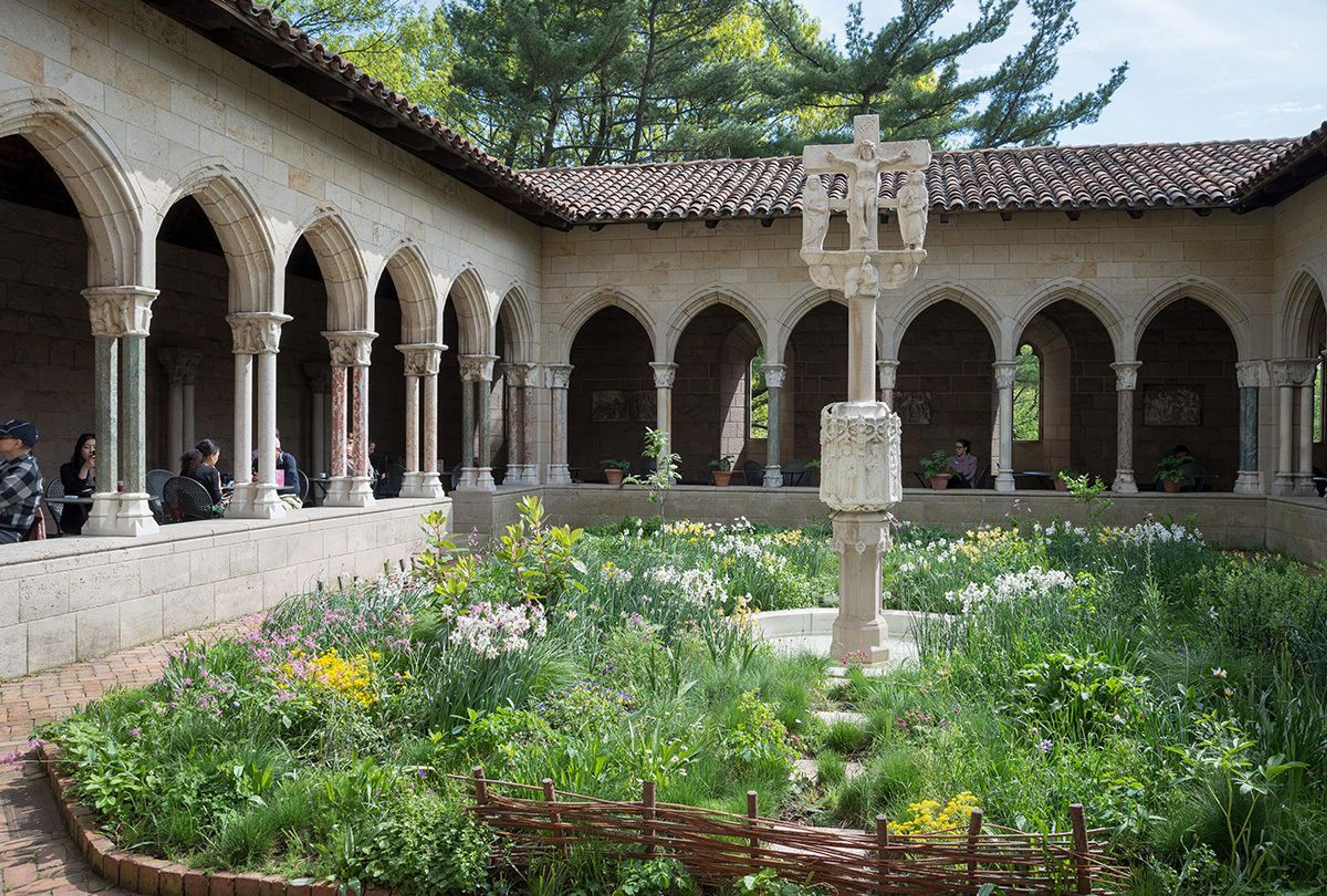 Patrons sit at tables and chairs in a stone arcade overlooking a garden.