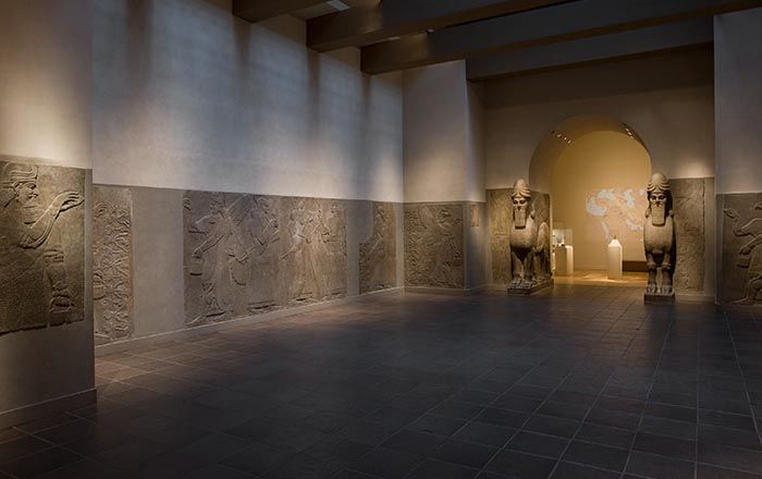 Room from an ancient Assyrian place decorated with large stone relief panels and colossal winged, human-headed animal deity sculptures