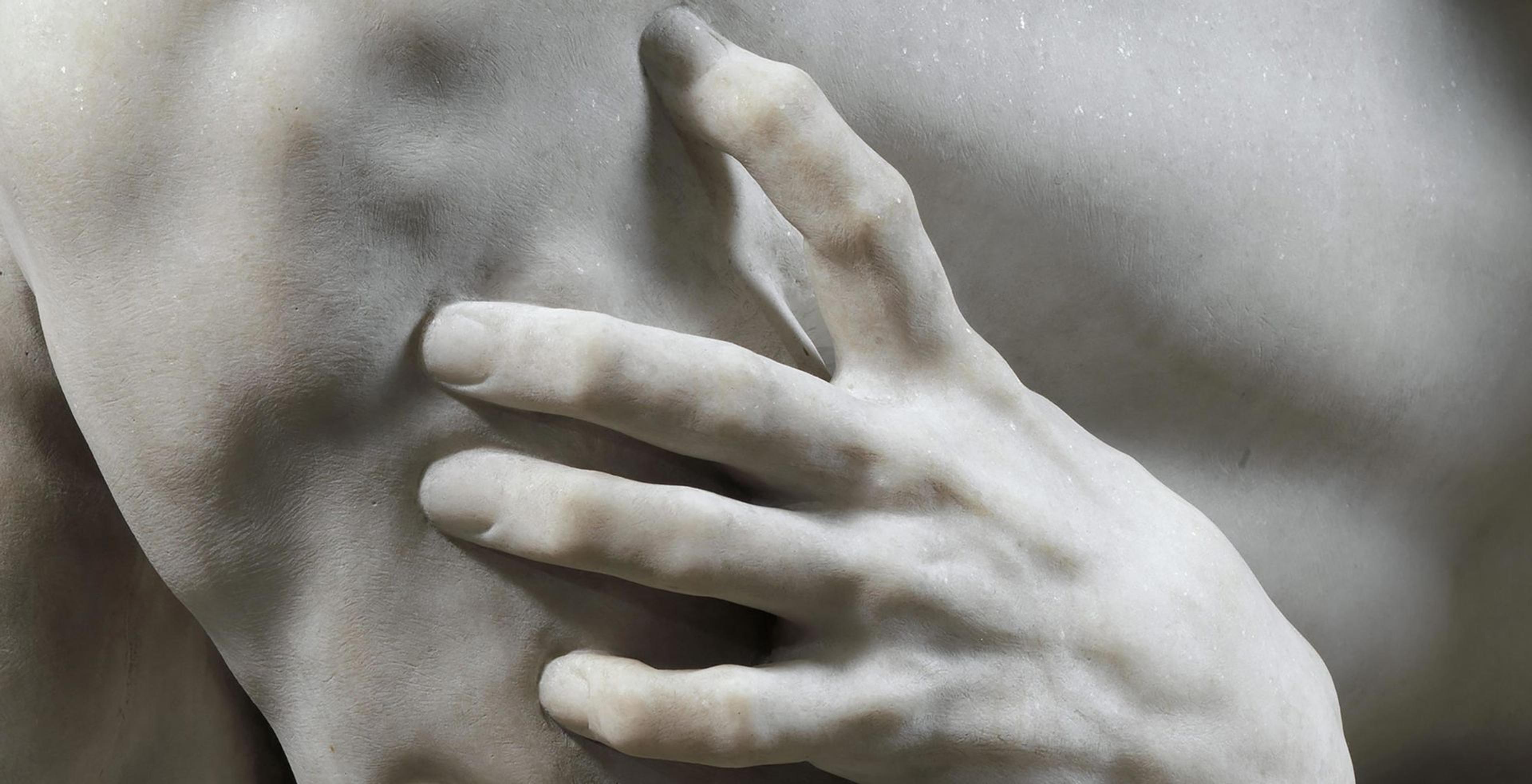 Detail view of a marble sculpture in which we see a hand grasping another piece of flesh
