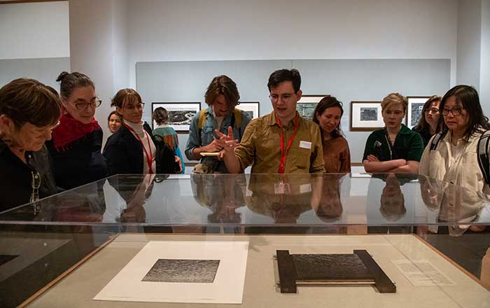 Fellows observe antiquated documents in a protective a glass cabinet in a museum gallery.
