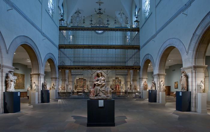 A very large gallery with a dark stone floor and central arcades subdividing the space for medieval Christian sculptures and church pieces