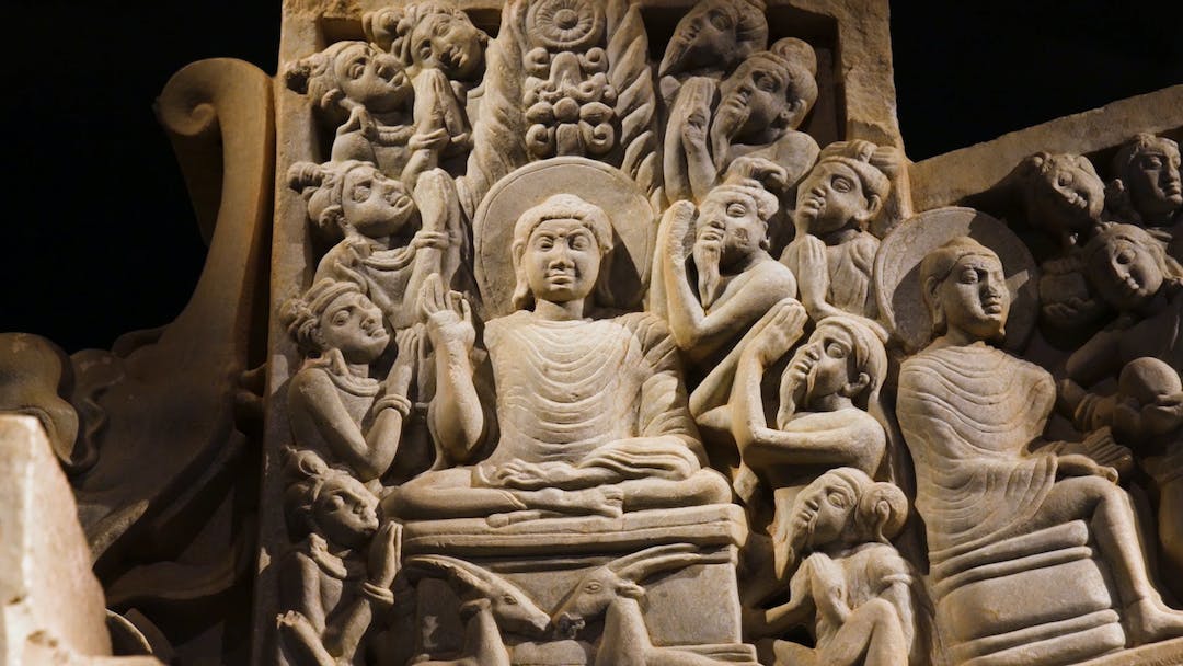 Medium frame of a large stone sculpture carved with the likeness of a seated Buddha surrounded by worshippers.