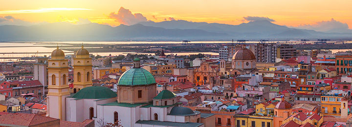 Panorama of a city with brightly colored rooftops and mountains in the background at sunset
